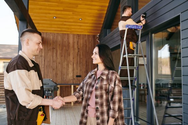 A man and a woman shaking hands after signing document against repairman